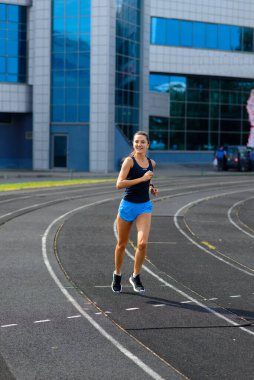 Stadyumda kollarını açarak ısınan sağlıklı genç bir kadın parkta koşu yapıyor..