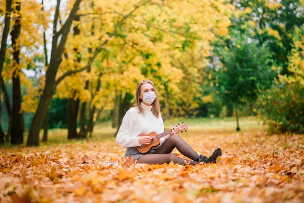 穿着防护面罩在秋天公园弹奏四弦琴的年轻女性形象 生活方式健康旅游理念 — 图库照片