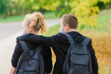 Okul çocukları, sağlık maskeli kız ve erkek çocuklar şehir parkında yürüyor..