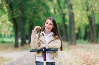 Güz parkında elektrikli scooter süren güzel bir kadın, ekolojik nakliye.