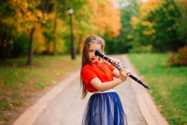 年轻迷人的姑娘在秋天的公园里玩单簧管 — 图库照片