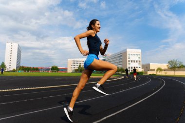 Sporcu atletizm pistinde koşuyor ve kardiyo çalışıyor. Kadınlar yaz stadyumunda yarışmak için koşuyorlar..