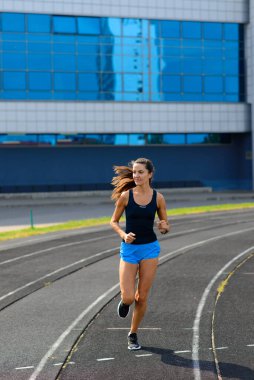 Sporcu atletizm pistinde koşuyor ve kardiyo çalışıyor. Kadınlar yaz stadyumunda yarışmak için koşuyorlar..