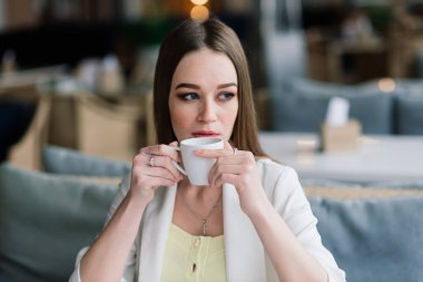 Beyaz ceketli genç bir kadın kafeteryada çalışıyor, kahve içiyor.