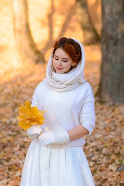 Uzun beyaz gelinlikli tatlı kız kırsal yolda poz veriyor ormandaki sonbahar ağaçları arasında altın saat atmosferinde.