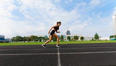 Sporcu atletizm pistinde koşuyor ve kardiyo çalışıyor. Kadınlar yaz stadyumunda yarışmak için koşuyorlar..