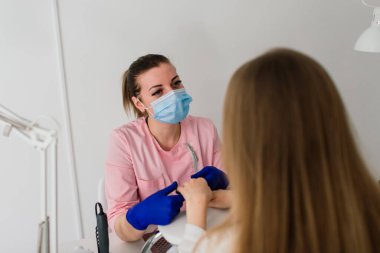 Güzellik salonunda kadın manikür ustası müşterinin elleriyle çalışıyor.