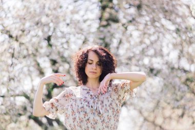 Bahar çiçekli bahçede poz veren kıvırcık saçlı çekici bir kadın.