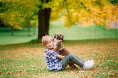 Çocuk köpeğe sarılıyor ve sonbaharda şehir parkında oynuyor.
