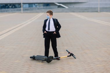 Şehirde scooter kullanan koruyucu maskeli tatlı bir okul çocuğu..