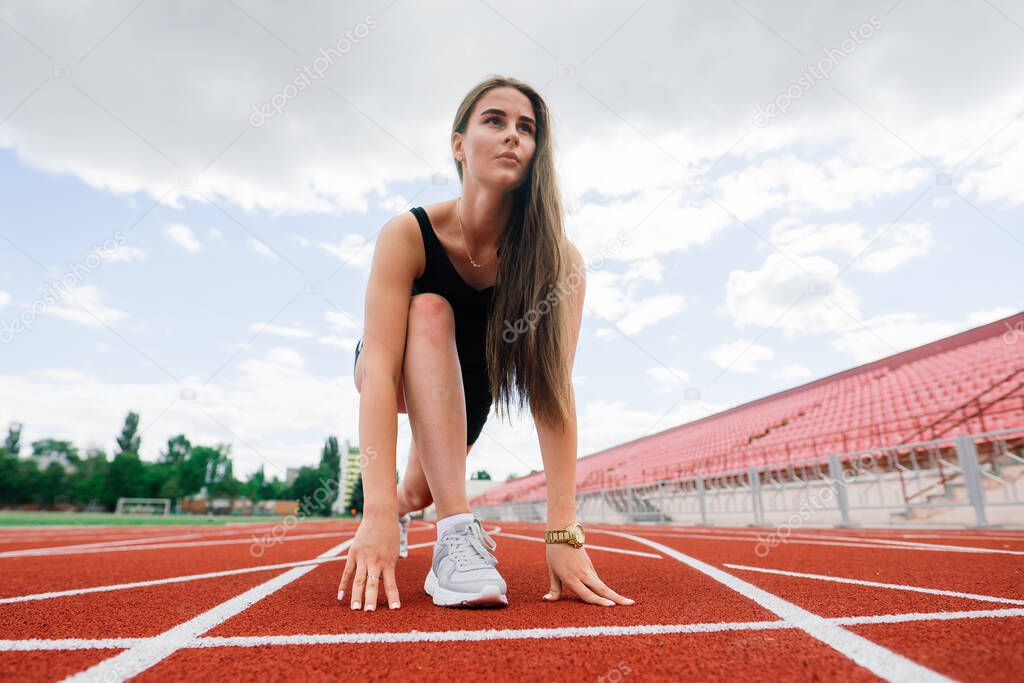 A female coach with dark hair stands on the red running track of the stadium, dressed in sports uniform.