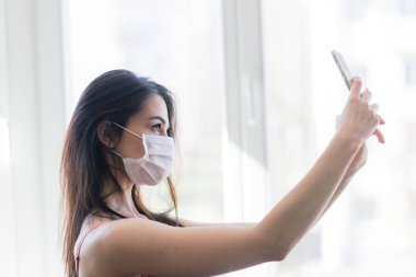 Karantinada güzel siyah saçlı kadın koruyucu maske takıyor ve evde çalışıyor.