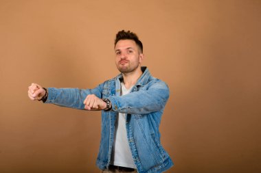 Yakışıklı adam ayakta ve gülümsüyor açık kahverengi stüdyo arka planında izole.