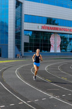 Sporcu atletizm pistinde koşuyor ve kardiyo çalışıyor. Kadınlar yaz stadyumunda yarışmak için koşuyorlar..
