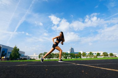 Sporcu atletizm pistinde koşuyor ve kardiyo çalışıyor. Kadınlar yaz stadyumunda yarışmak için koşuyorlar..