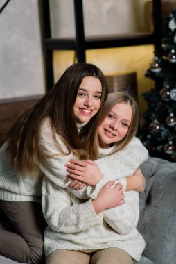 İki tatlı kız bir Noel ağacıyla birlikte bir kanepede oturuyor. Yeni yıl konsepti