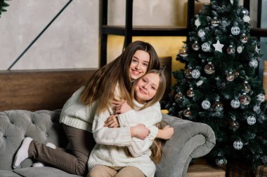 İki tatlı kız bir Noel ağacıyla birlikte bir kanepede oturuyor. Yeni yıl konsepti