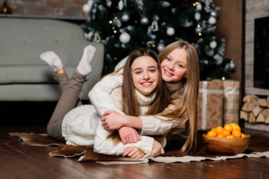 İki tatlı kız bir Noel ağacıyla birlikte bir kanepede oturuyor. Yeni yıl konsepti