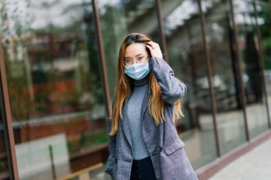 Yüz maskesi takan Asyalı genç bir kadın yerel bir caddede duruyor..