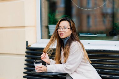 Güzel genç Çinli öğrenci sokakta bir fincan kahve tutuyor.