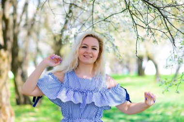 Belini kaldır ve çiçek açan erik ağacının yanında sarı saçlı, gülümseyen genç bir kadının yakın portresini çek.