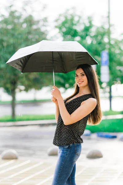Portrait of a happy woman wearing jeans under an umbrella smiling in the street in rainy day