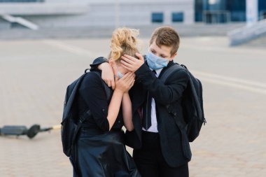 Eğitim, çocukluk ve insan kavramı. Dışarıda koruyucu maskeli sırt çantalı ve scooterlı çocuklar.