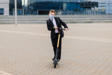 Şehirde scooter kullanan koruyucu maskeli tatlı bir okul çocuğu..