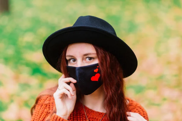 穿着针织红毛衣 头戴黑色时髦口罩的年轻女子在秋天的黄色公园里的画像 生活方式 — 图库照片