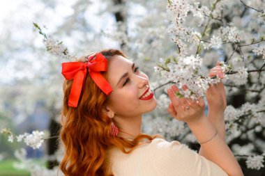 Bahar çiçekleri içinde beyaz elbiseli güzel kızıl saçlı genç kadının portresi.