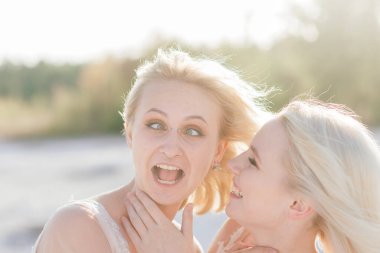 Sarışın, beyaz elbiseli iki gelin birbirlerine sarılıyorlar, lezbiyen düğünü.