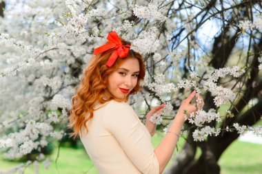 Bahar çiçekleri içinde beyaz elbiseli güzel kızıl saçlı genç kadının portresi.