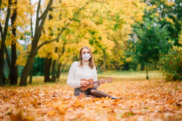 穿着防护面罩在秋天公园弹奏四弦琴的年轻女性形象 生活方式健康旅游理念 — 图库照片