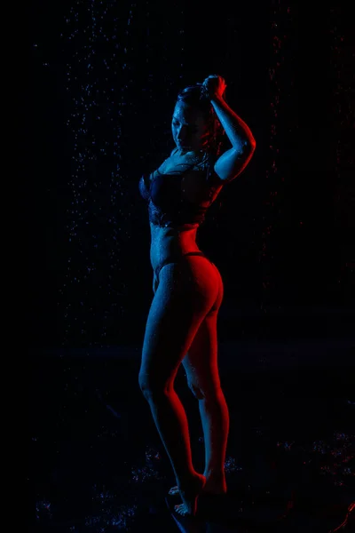 小さなプールで水と写真撮影中に光に照らされた暗い部屋に水滴と白いシャツの女性 — ストック写真