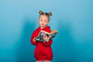 Küçük anaokulu çocuğu mavi üzerine izole bir şekilde kitap okurken öğreniyor.