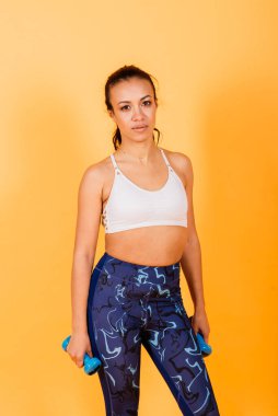 Güç ve motivasyon. Stüdyoda sarı arka planda spor kıyafetleriyle egzersiz yapan zayıf ve uzun boylu Afrikalı bir kadın.