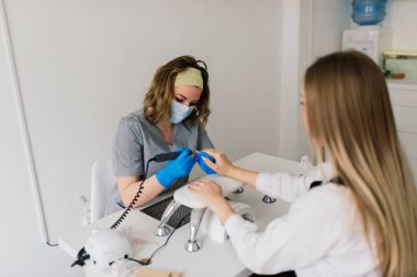 Güzellik salonunda kadın manikür ustası müşterinin elleriyle çalışıyor.