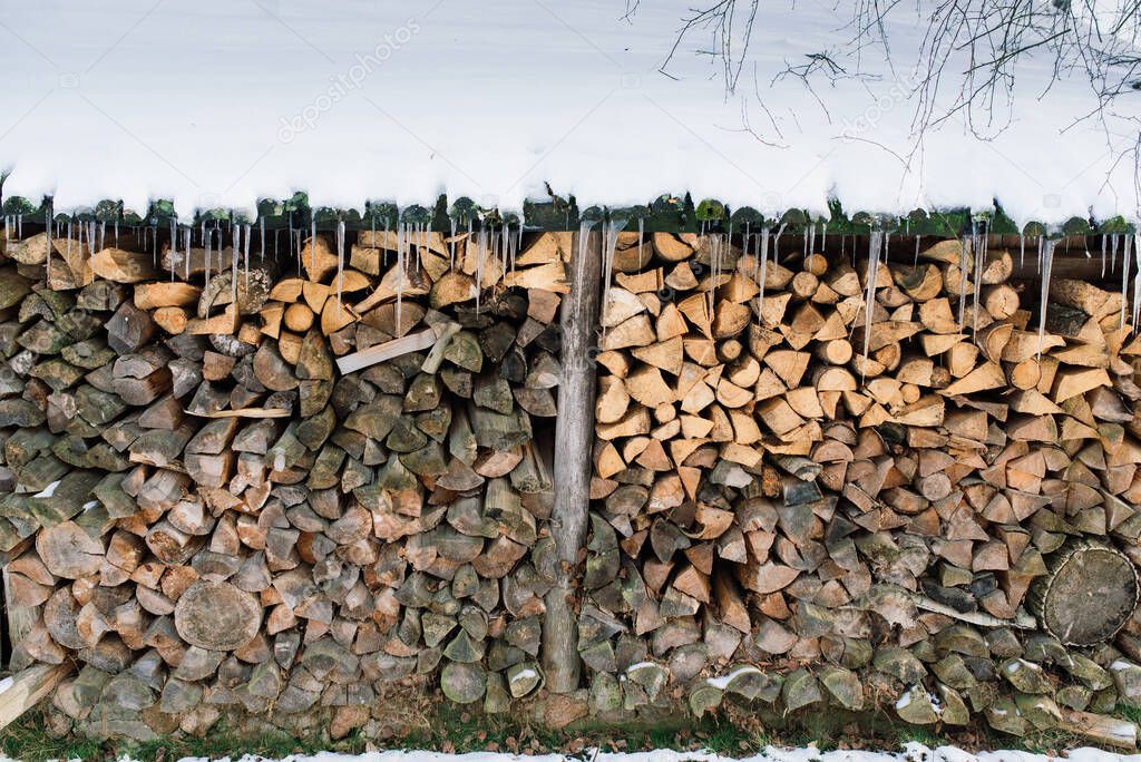 Woodpile of firewood on the outskirts of a farm, yard and winter forest