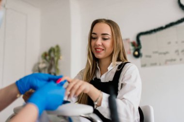 Güzellik salonunda kadın manikür ustası müşterinin elleriyle çalışıyor.