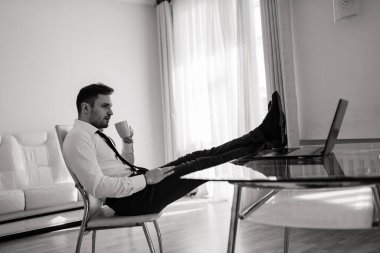 İş adamı gömleğini giyip ofiste bilgisayardan video görüşmesi yapıyor.