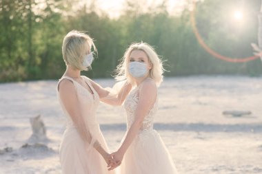 Lezbiyen çift beyaz kumda evleniyor, salgın COVID-19 'u önlemek için maske takıyorlar.