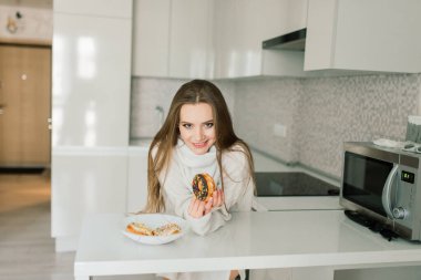 Bir fincan kahve, akıllı telefon ve yatakta keklerle çekici bir kadın.