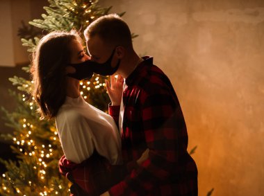 2021 yılını ev karantinasında kutlayan maskeli çekici bir adam ve genç kadın, tecrit. Madalyalı Noel ağacı ve balonlar.