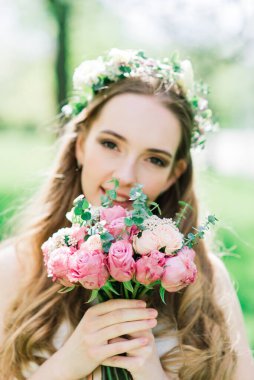 Beyaz gelinlikli gelin yeşil parkta bir buket tutuyor. Güneşli bir günde yaz düğünü..