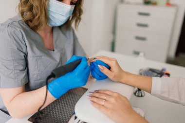 Güzellik salonunda kadın manikür ustası müşterinin elleriyle çalışıyor.