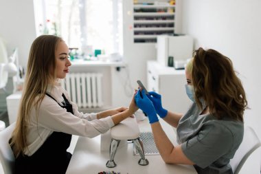 Güzellik salonunda kadın manikür ustası müşterinin elleriyle çalışıyor.