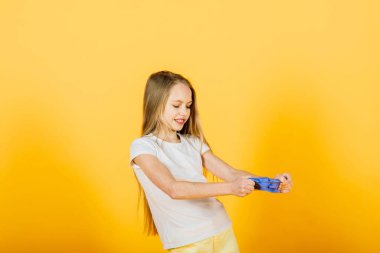 Sarı arka planda mavi sümükle oynayan genç kız, stüdyo çekimi.