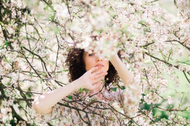 Bahar çiçekli bahçede poz veren kıvırcık saçlı çekici bir kadın.