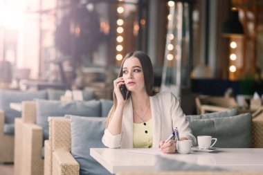 Beyaz ceketli genç bir kadın kafeteryada çalışıyor, kahve içiyor.