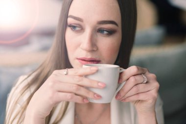 Beyaz ceketli genç bir kadın kafeteryada çalışıyor, kahve içiyor.
